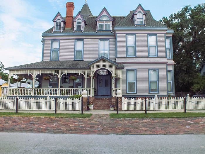 A large Victorian-style house with a porch and a white picket fence.